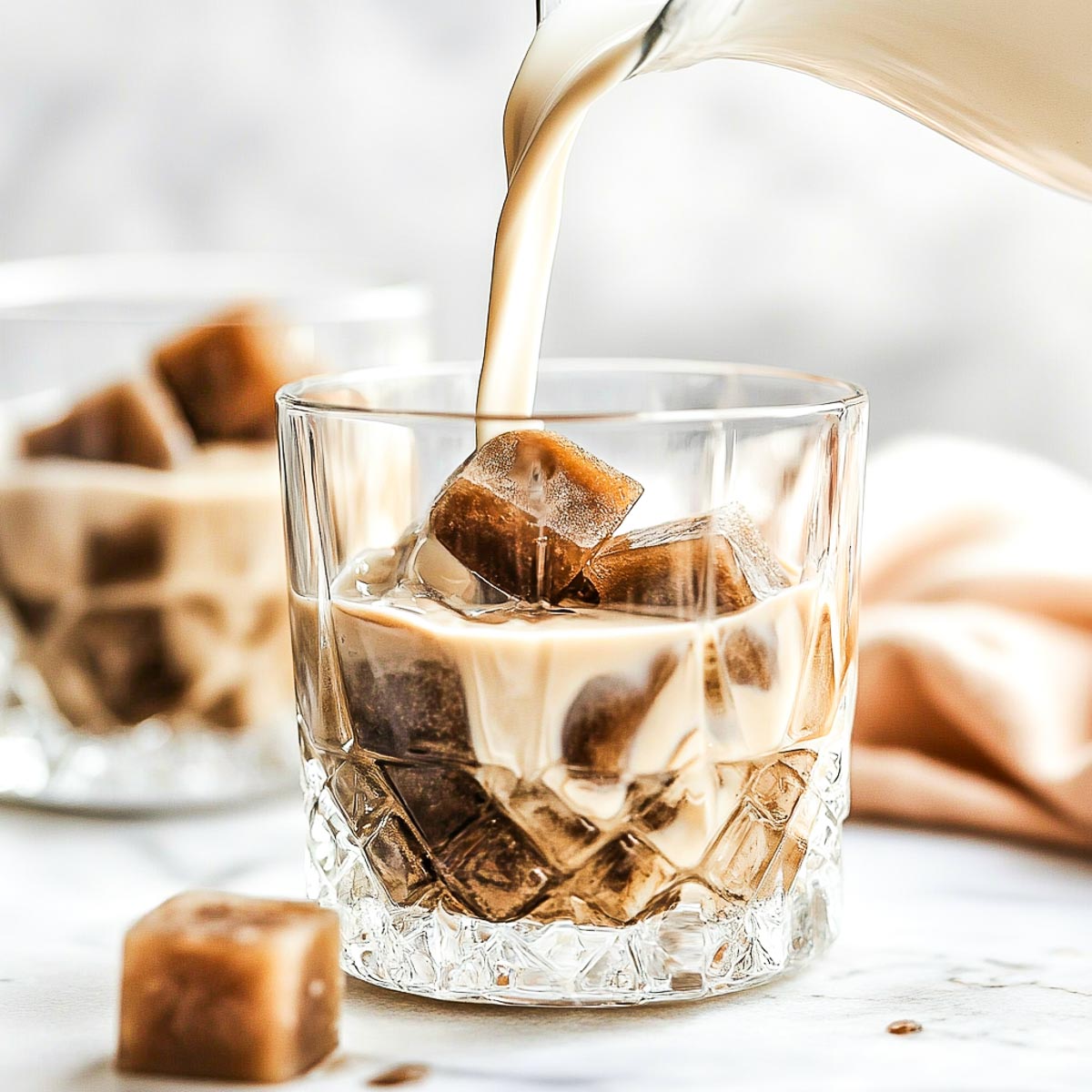 Ice cubes in a glass with milk being poured from the top.
