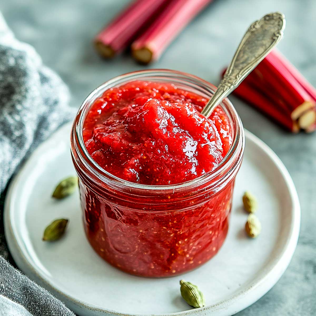 Rhubarb cardamom jam in a glass jar placed on a small white plate.