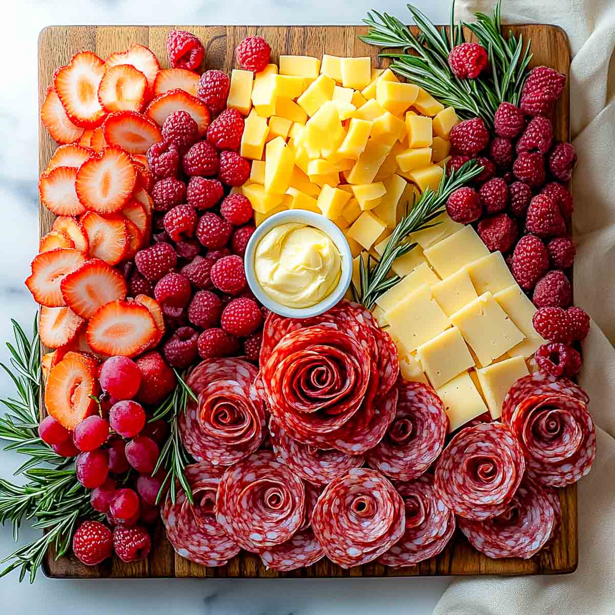 A charcuterie board with fruits, cheese, honey butter and salami roses.