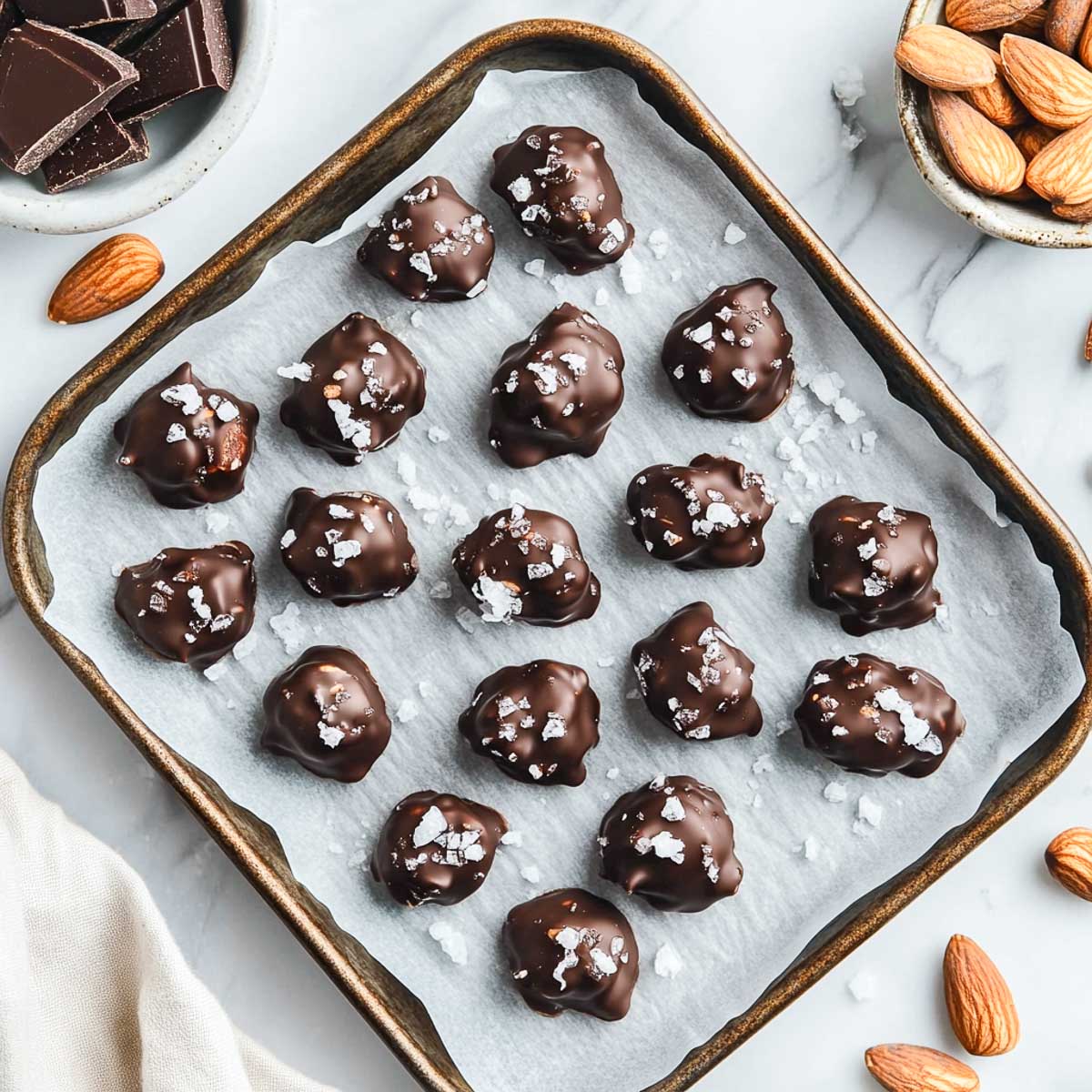 Dark chocolate-covered almond clusters on a lined baking tray.
