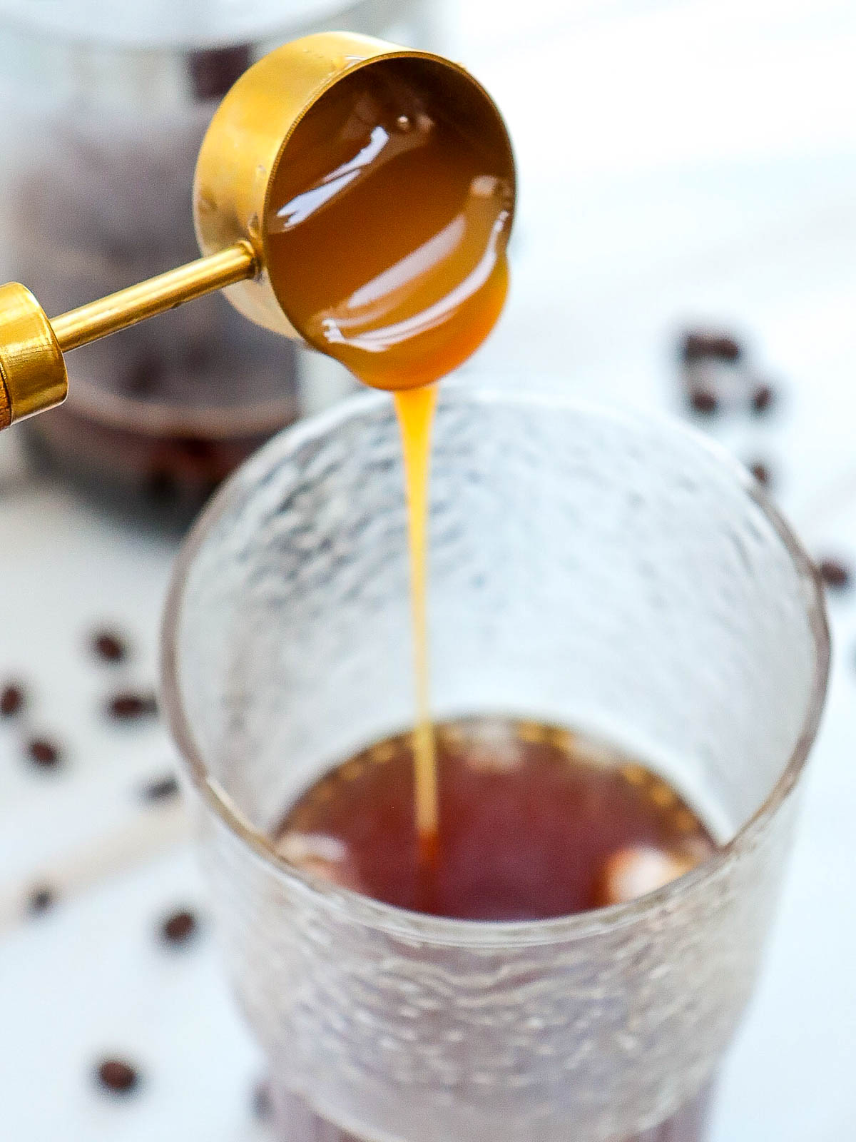 Caramel being poured into a glass with coffe and ice cubes in it.