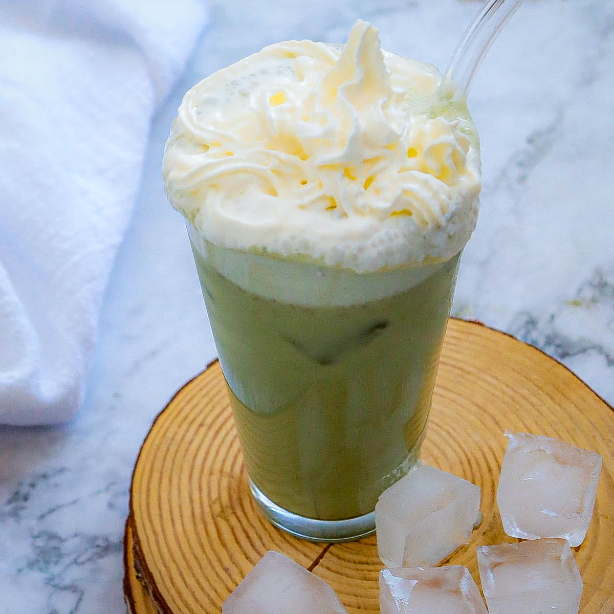Slightly angled view of a glass of green tea frappuccino with some ice in the background.