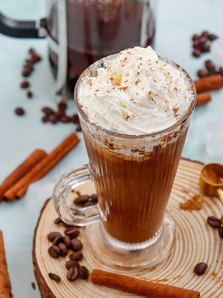 Iced cinnamon dolce latte glass with French coffee press on the background.