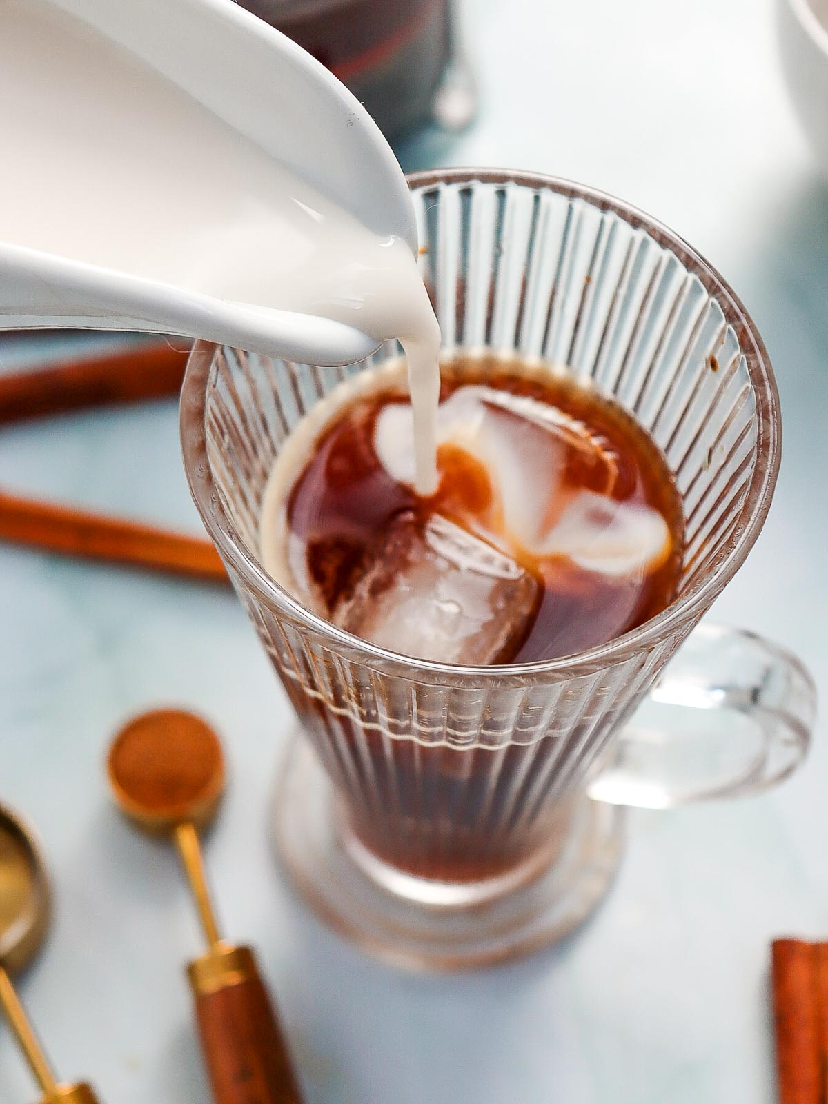 Milk being poured over brewed coffee in a tall glass.