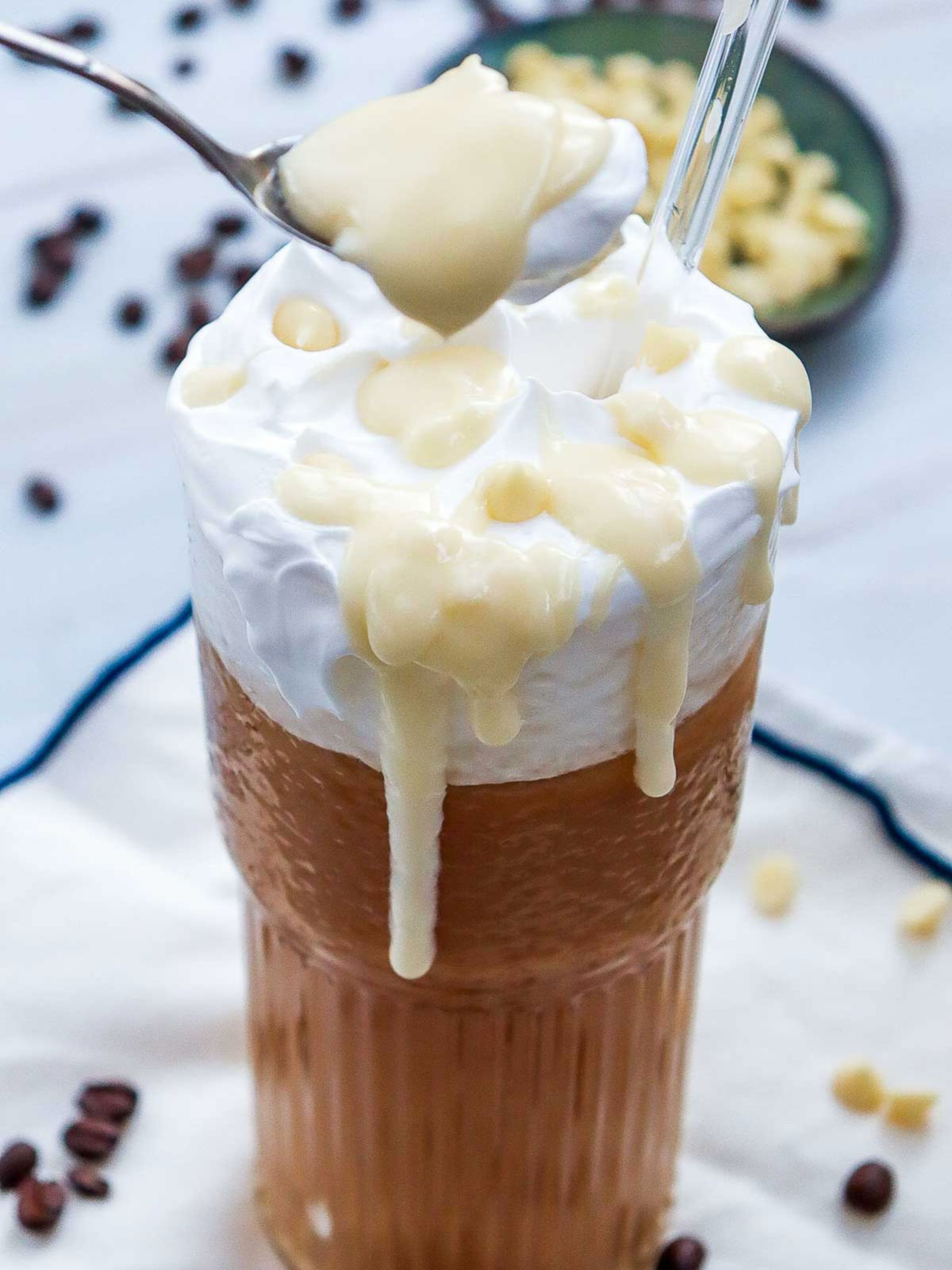A spoon scooping syrup and cream from iced white chocolate mocha glass.