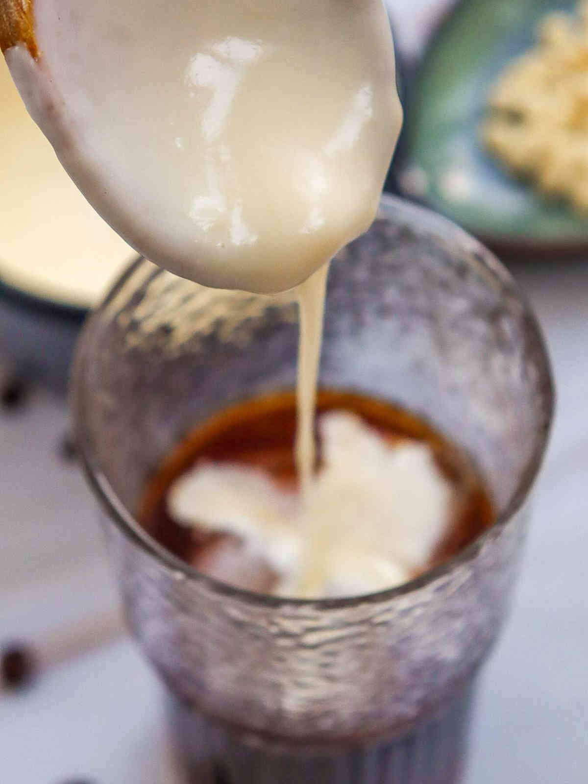 Homemade syrup poured on brewed coffee in a glass.
