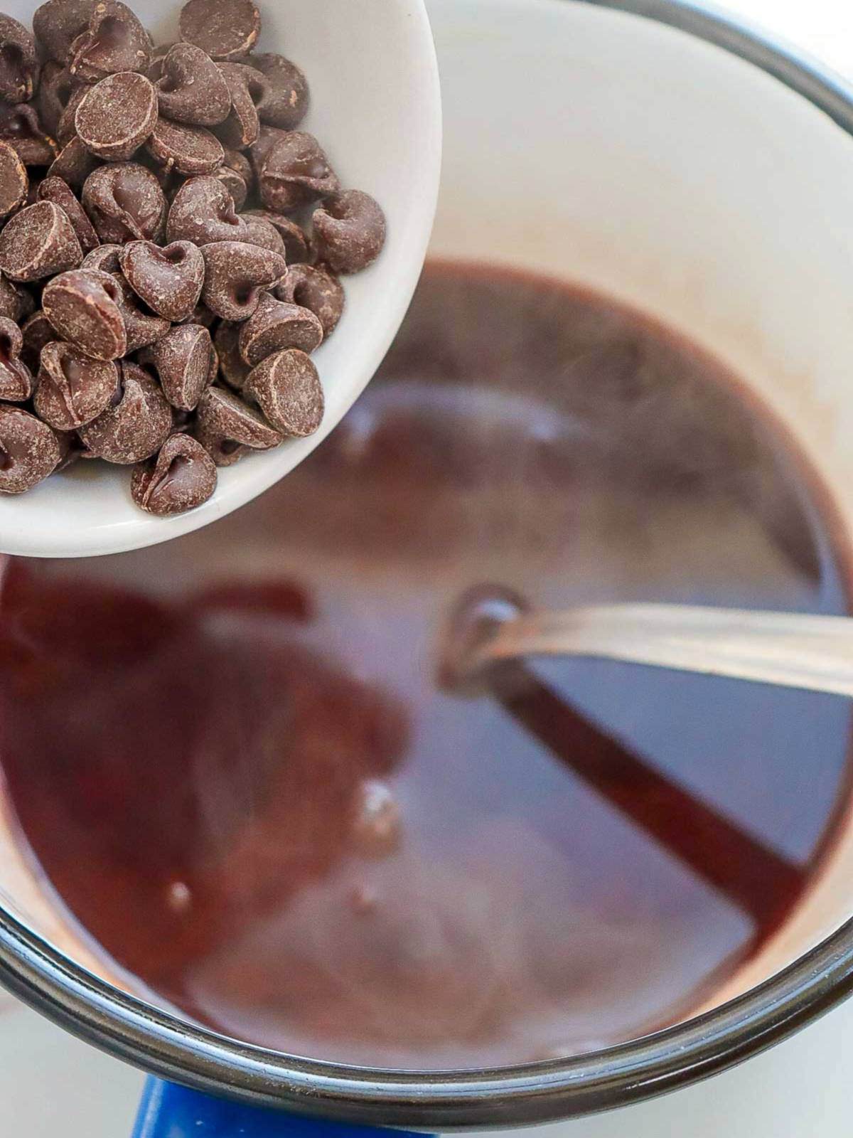 Chocolate chips being added to the sauce pan with warm milk and cocoa powder.