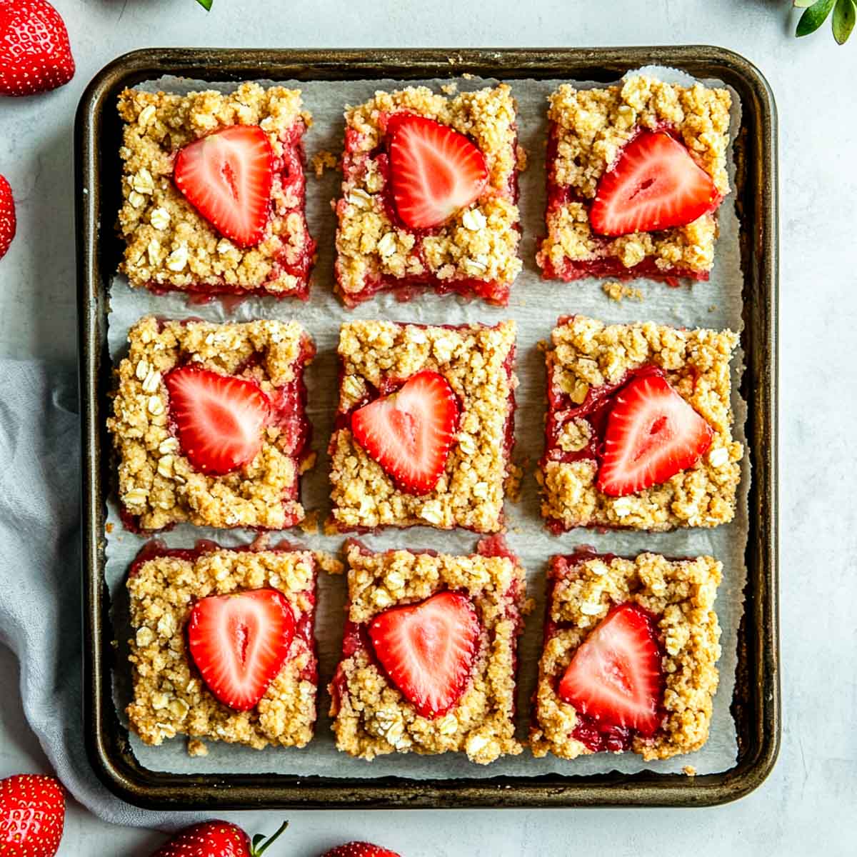 Strawberry rhubarb bars on a baking tray placed on a white marble surface.