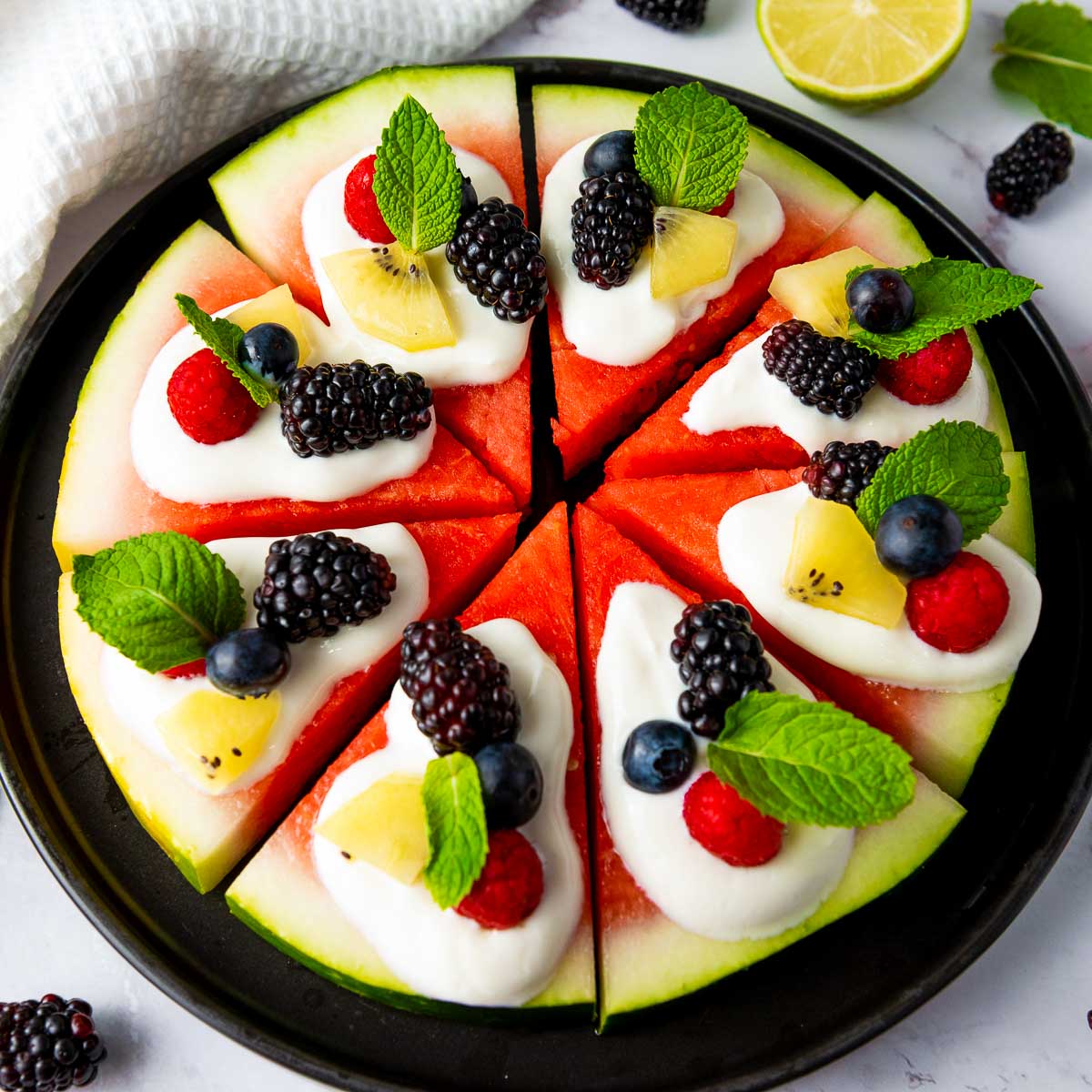 Close up of watermelon pizza on a black plate.
