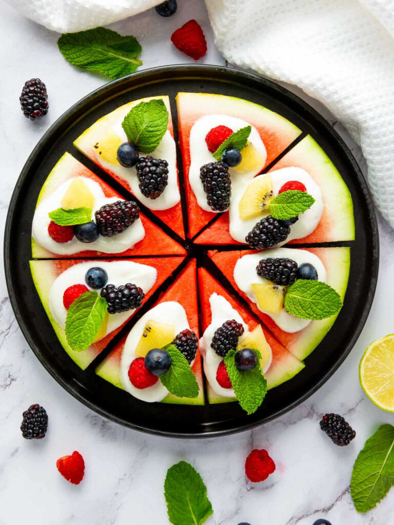 Watermelon pizza with fruit toppings garnished with mint leaves.