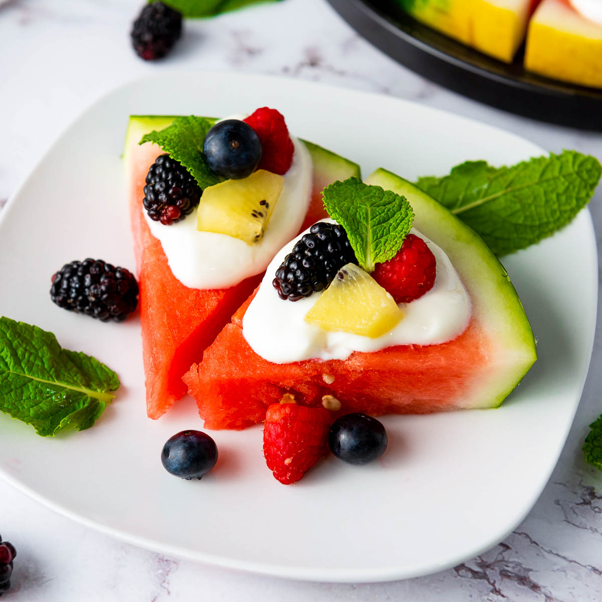 Two slices of watermelon pizza served with berries on a white plate.