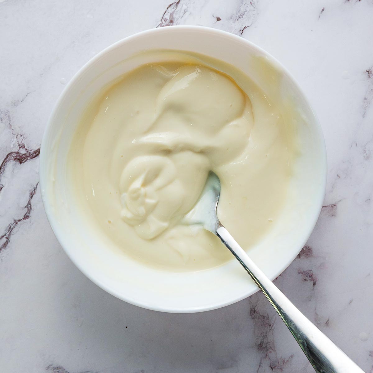 Honey yogurt sauce in a white bowl placed on a marble surface.