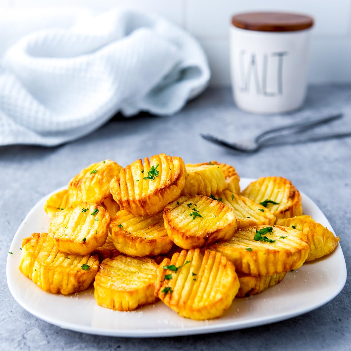Accordion potatoes on a white plate with salt box in the background.