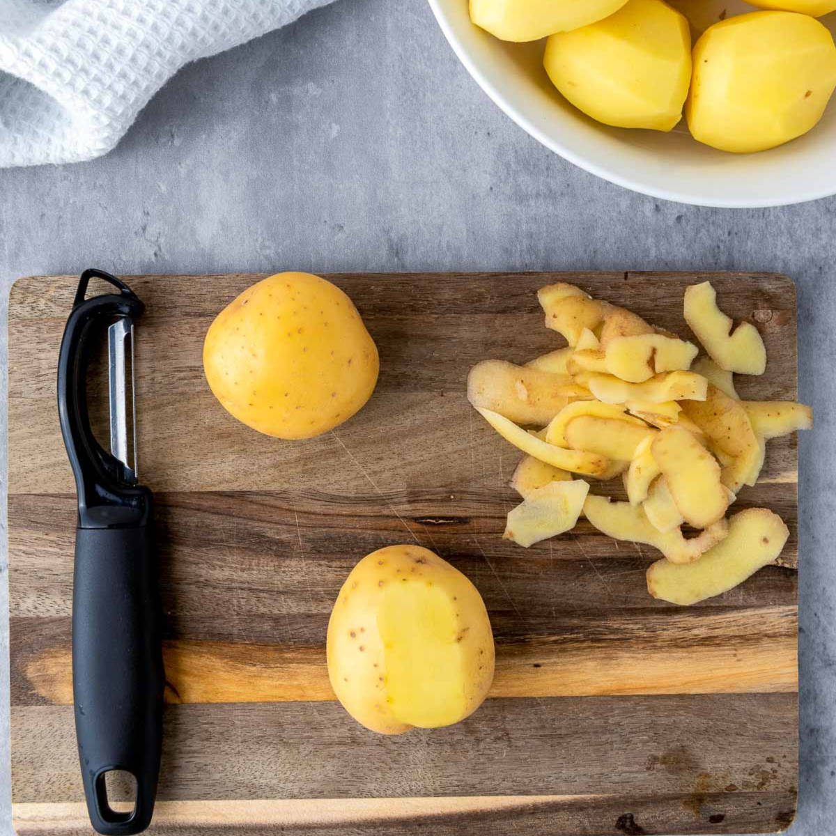 Washed and peeled potatoes on a wooden cutting board.