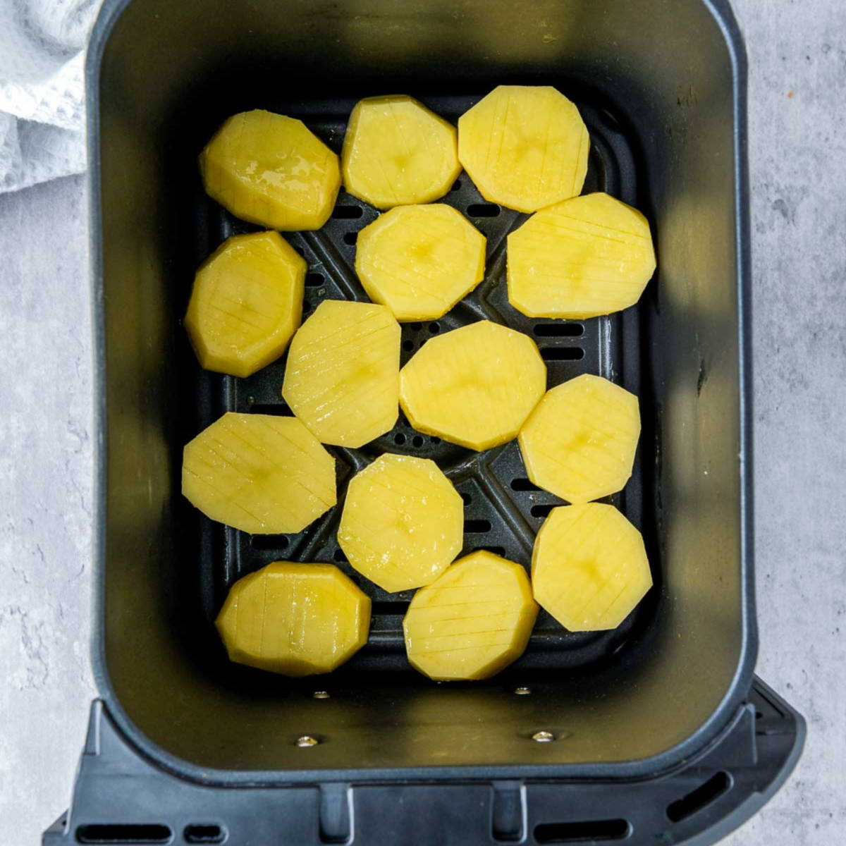 Sliced potatoes placed in air fryer basket.