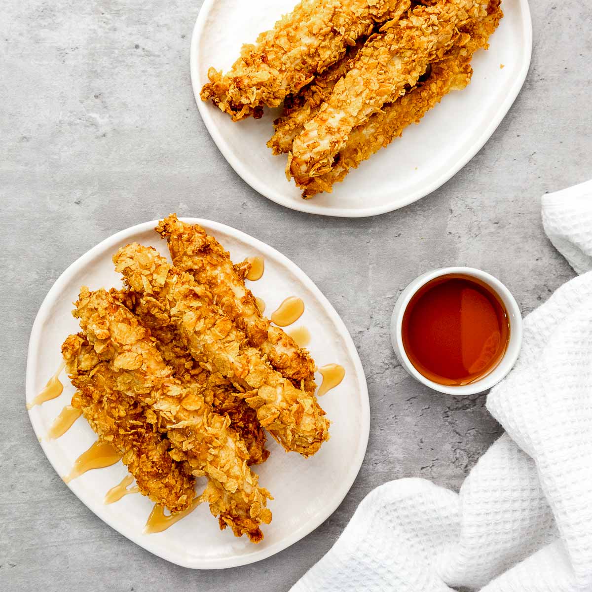 Cornflake chicken served on a white plate and drizzled with hot honey.