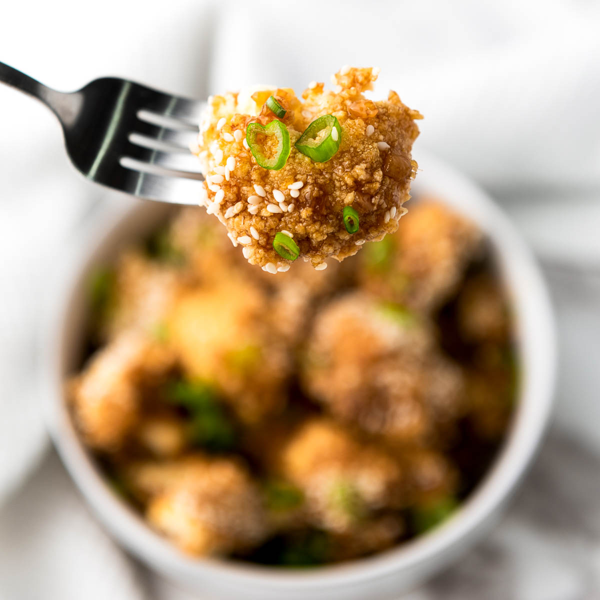Teriyaki caulilower on a fork over the serving bowl.