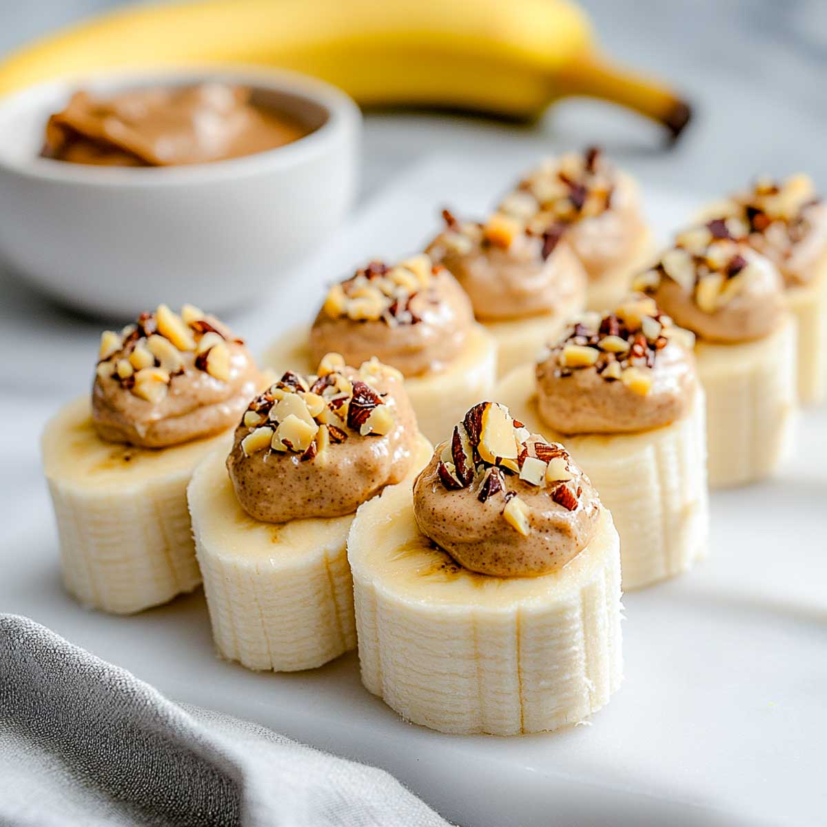 Banana slices topped with almond butter and chopped nuts on white plate