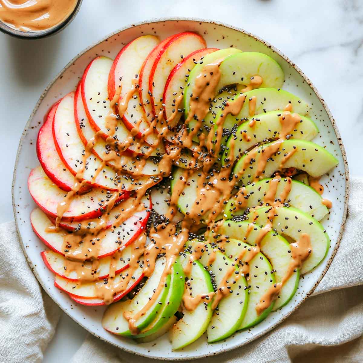 Thin apple slices drizzled with peanut butter and sprinkled with chia seeds.