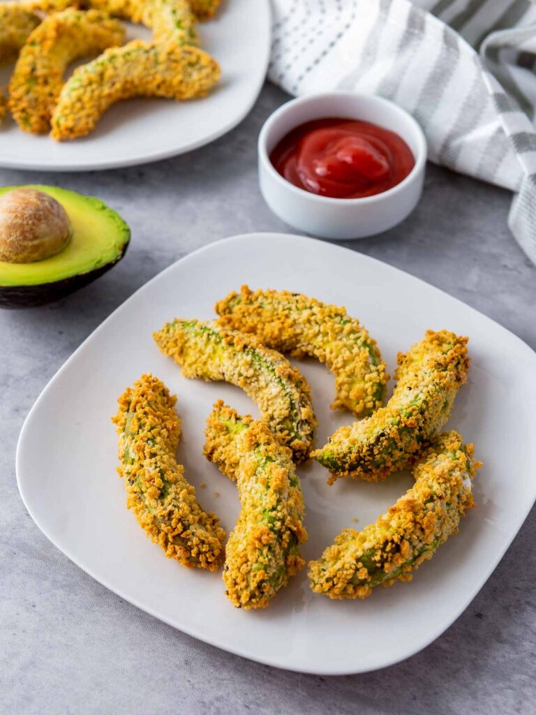 Two plates of air fryer avocado fries placed on a grey surface.