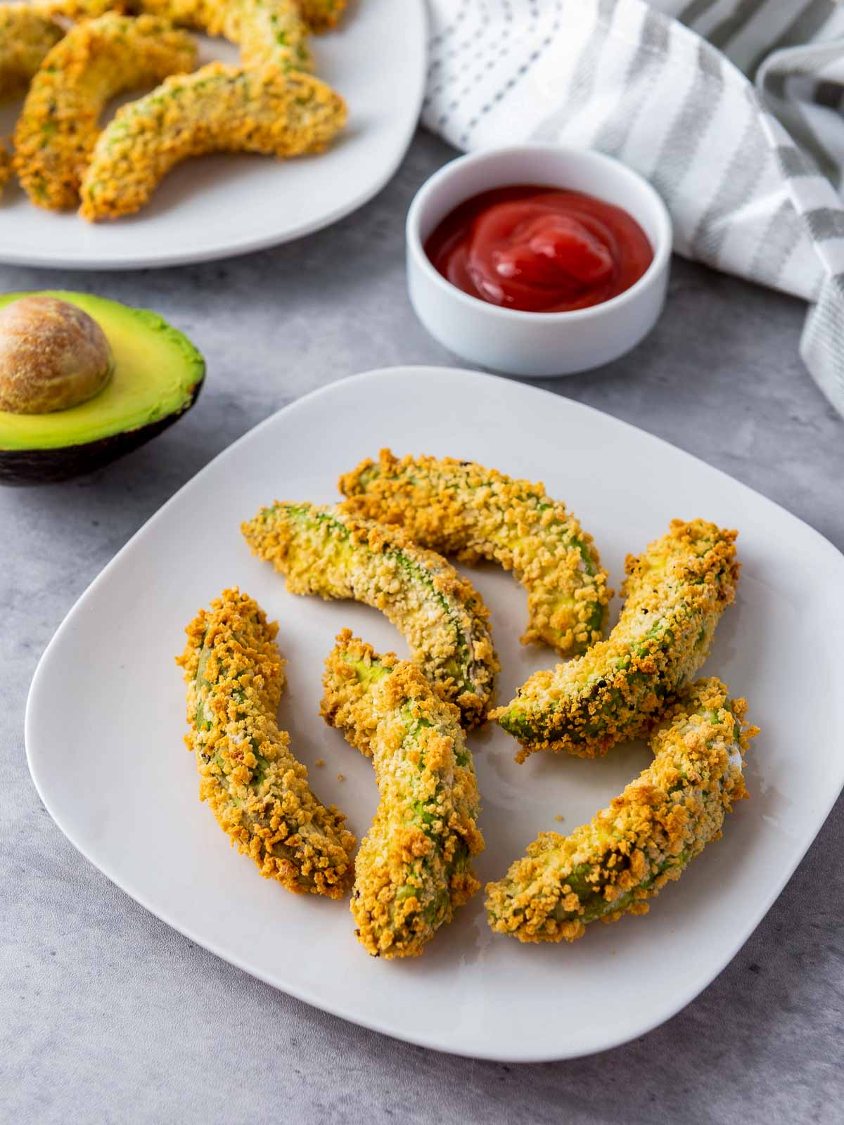 Two plates of air fryer avocado fries placed on a grey surface.