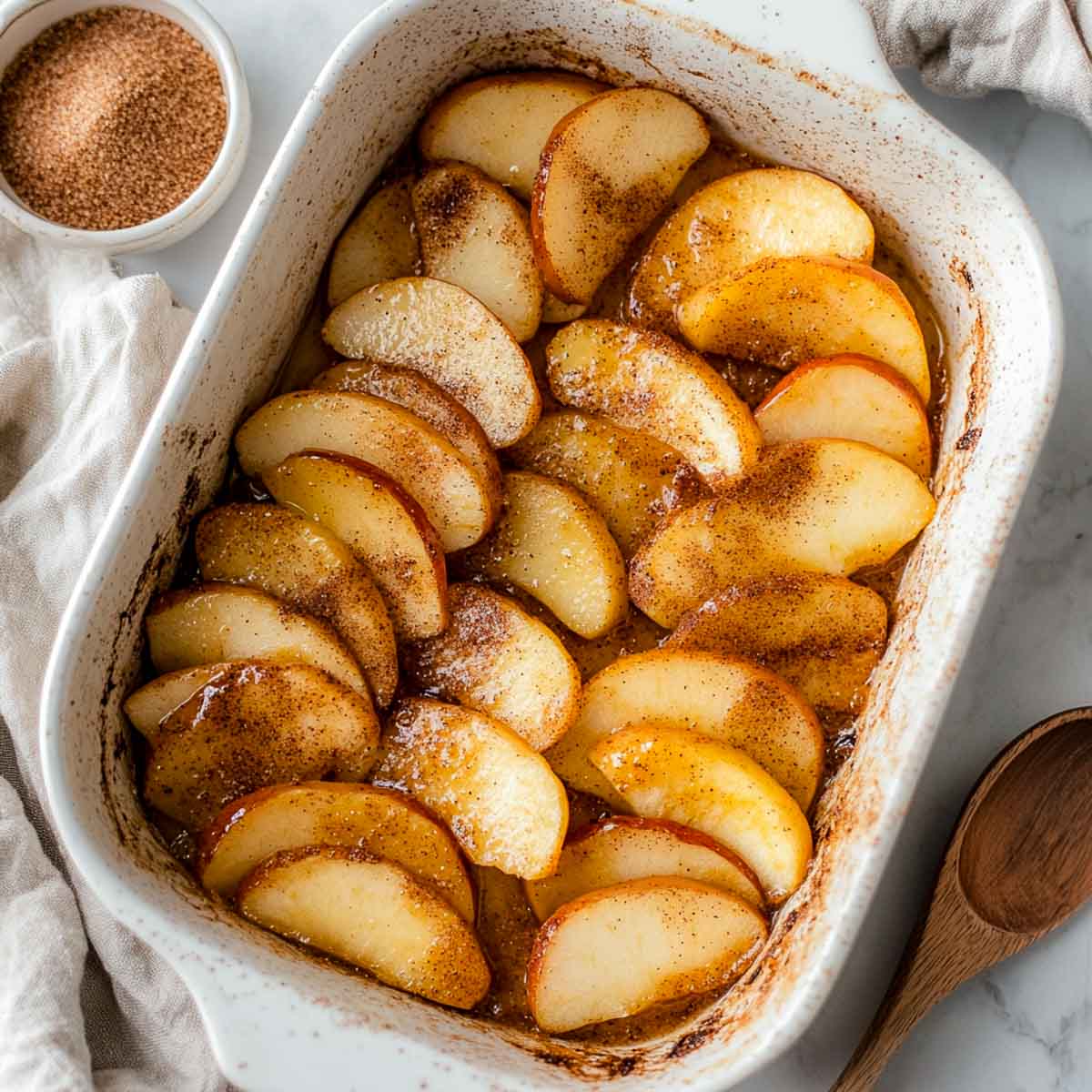 Top-down shot of baked apple slices layered in a rectangular white baking dish.