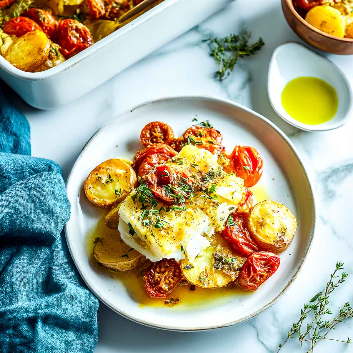 Flaky baked cod with potatoes and tomatoes, topped with herbs and olive oil.