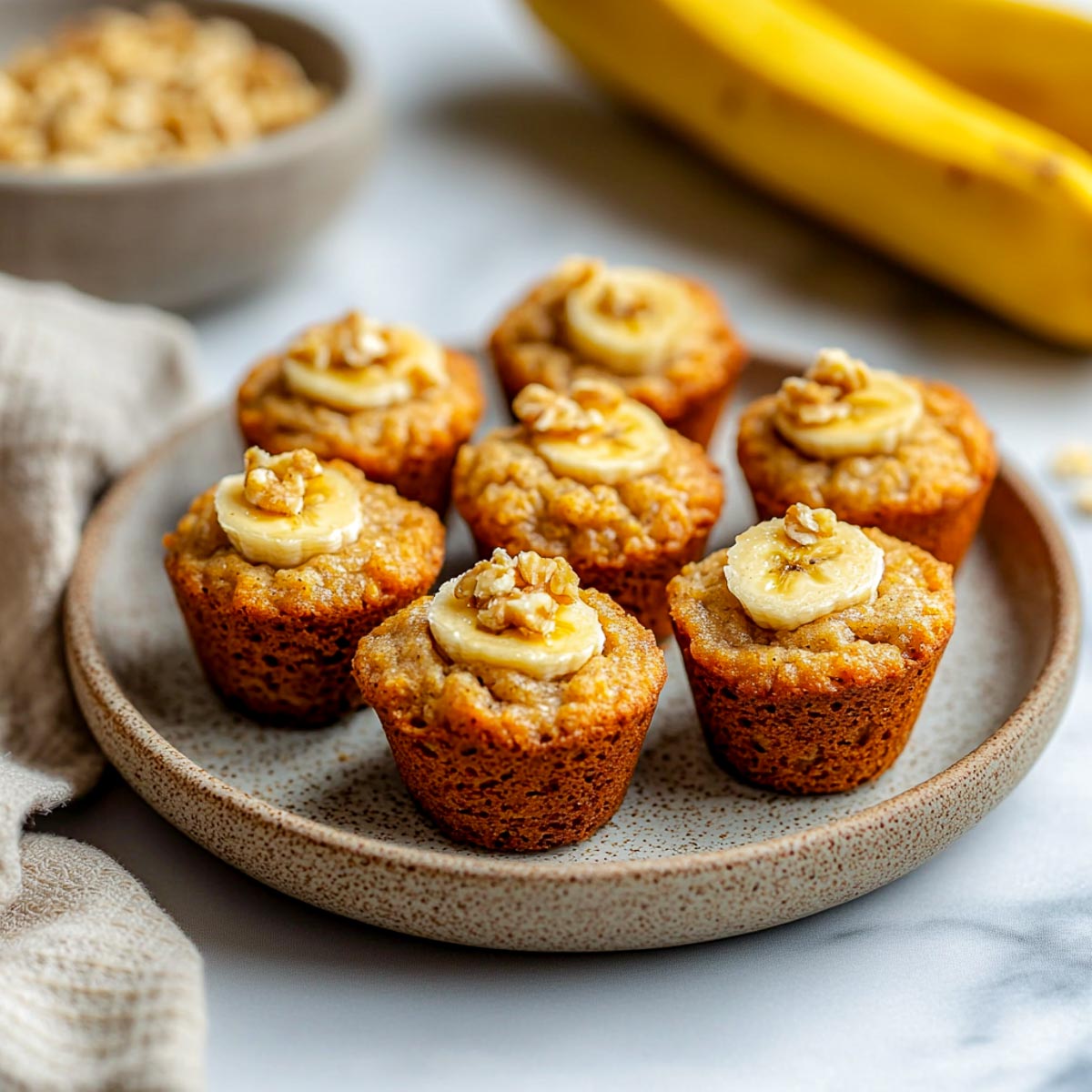 Mini banana bread bites topped with banana slices and walnuts on a ceramic plate.