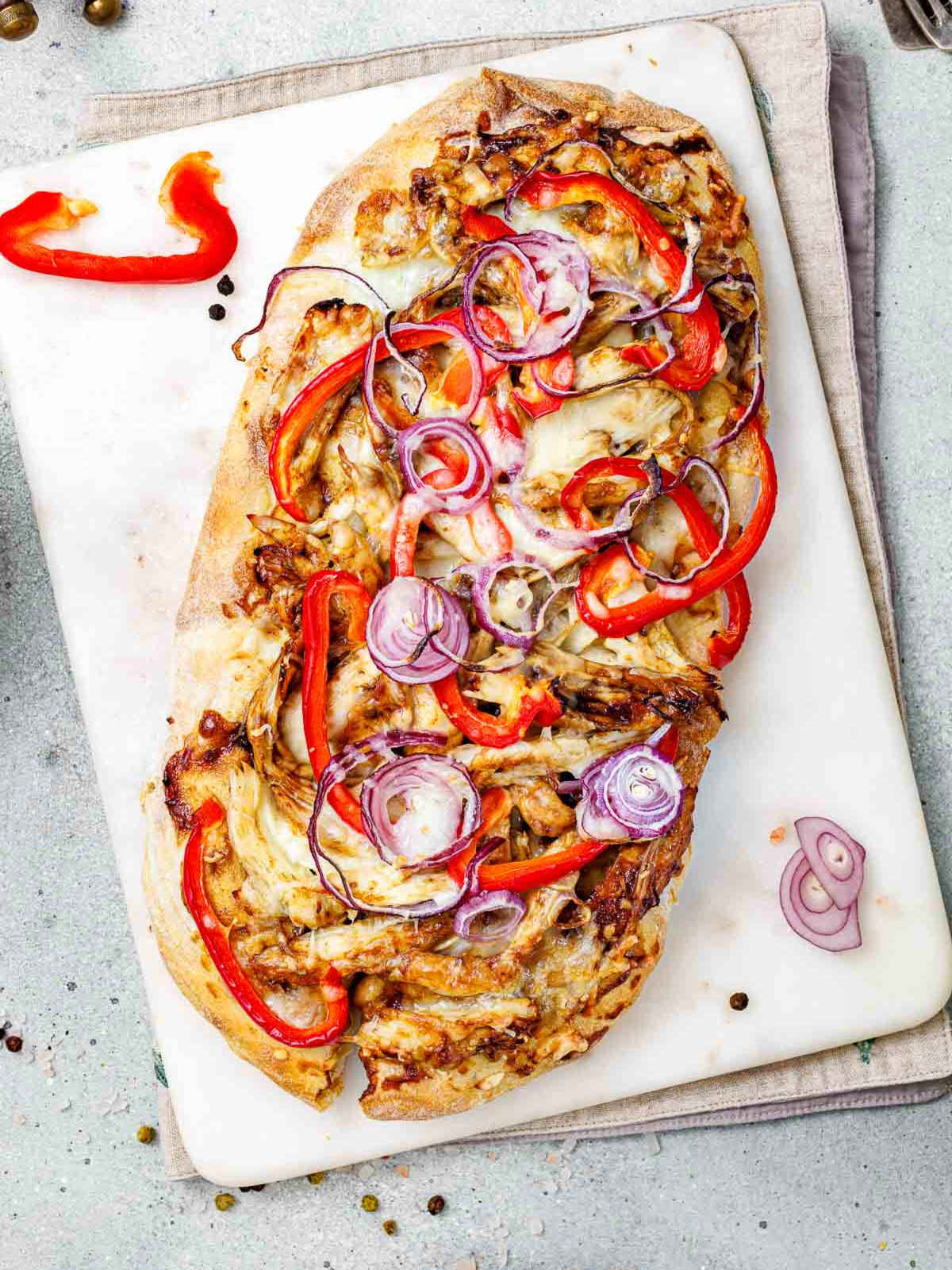 Close up of bbq chicken flatbread placed on a white surface.