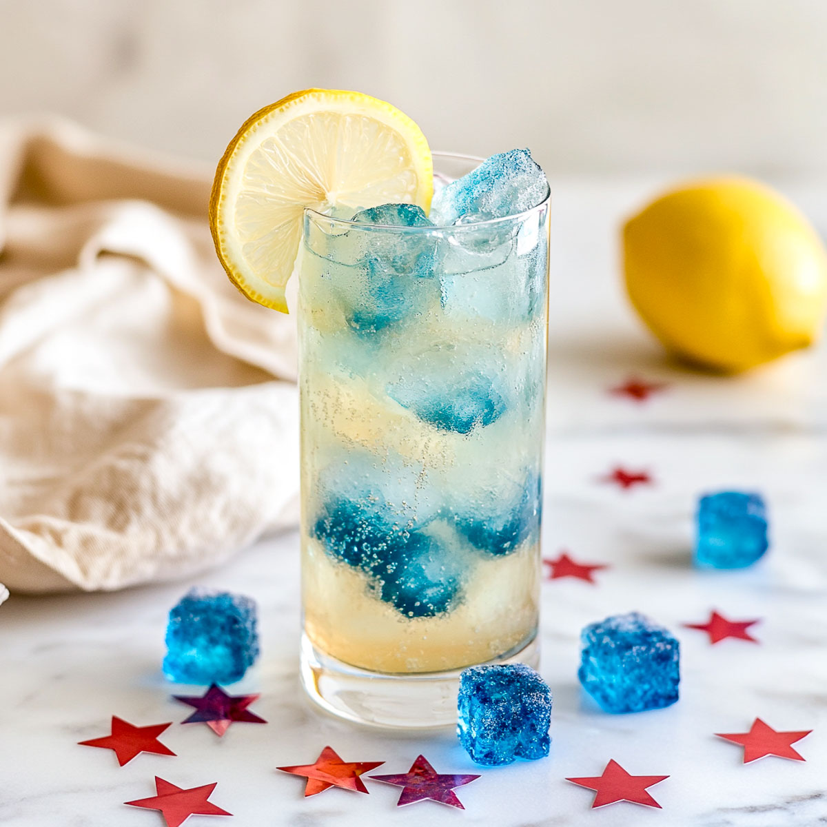 Tall glass of lemonade with blue raspberry ice cubes and star confetti.