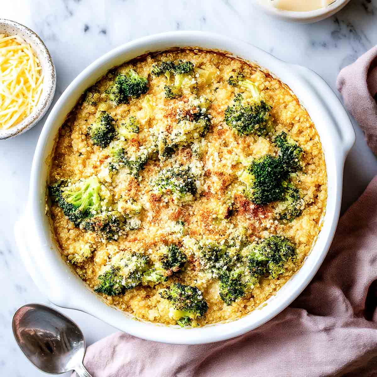Broccoli quinoa casserole with melted cheese and breadcrumbs in white baking dish.