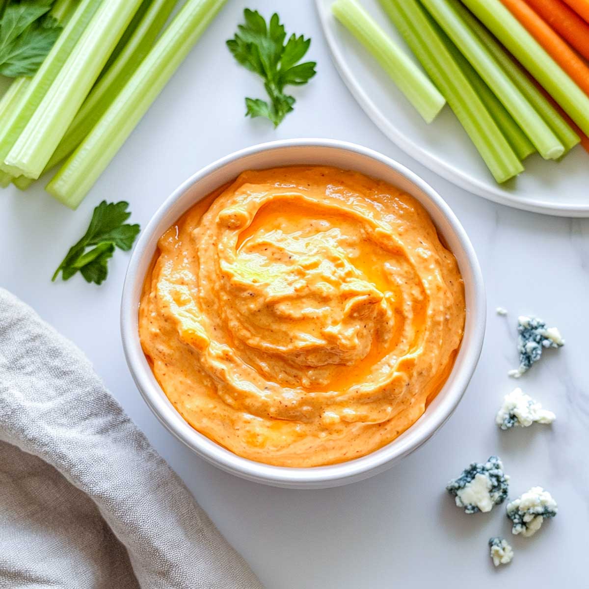 Buffalo Greek yogurt dip with celery sticks, carrot sticks, and blue cheese crumbles.