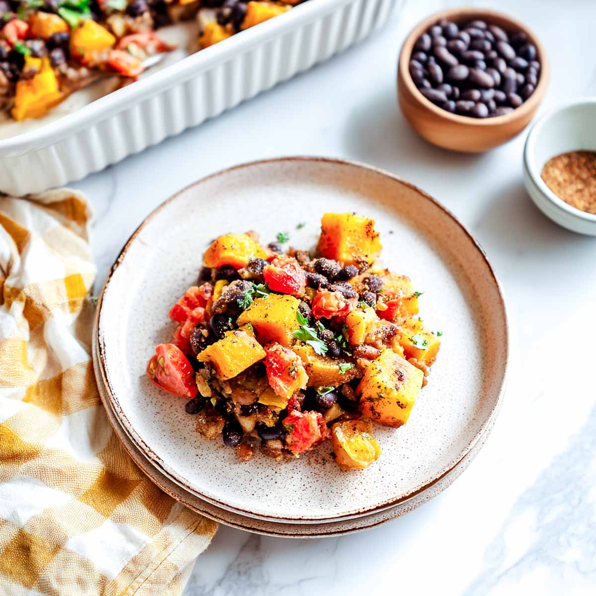 Roasted butternut squash and black bean casserole served on a plate with cozy napkin.