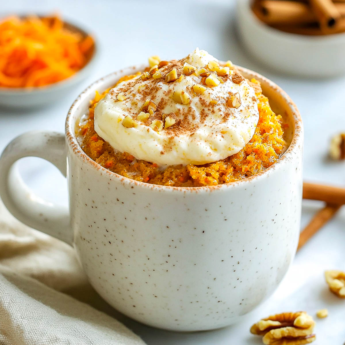 Carrot cake mug cake topped with frosting and walnuts in white mug on marble.