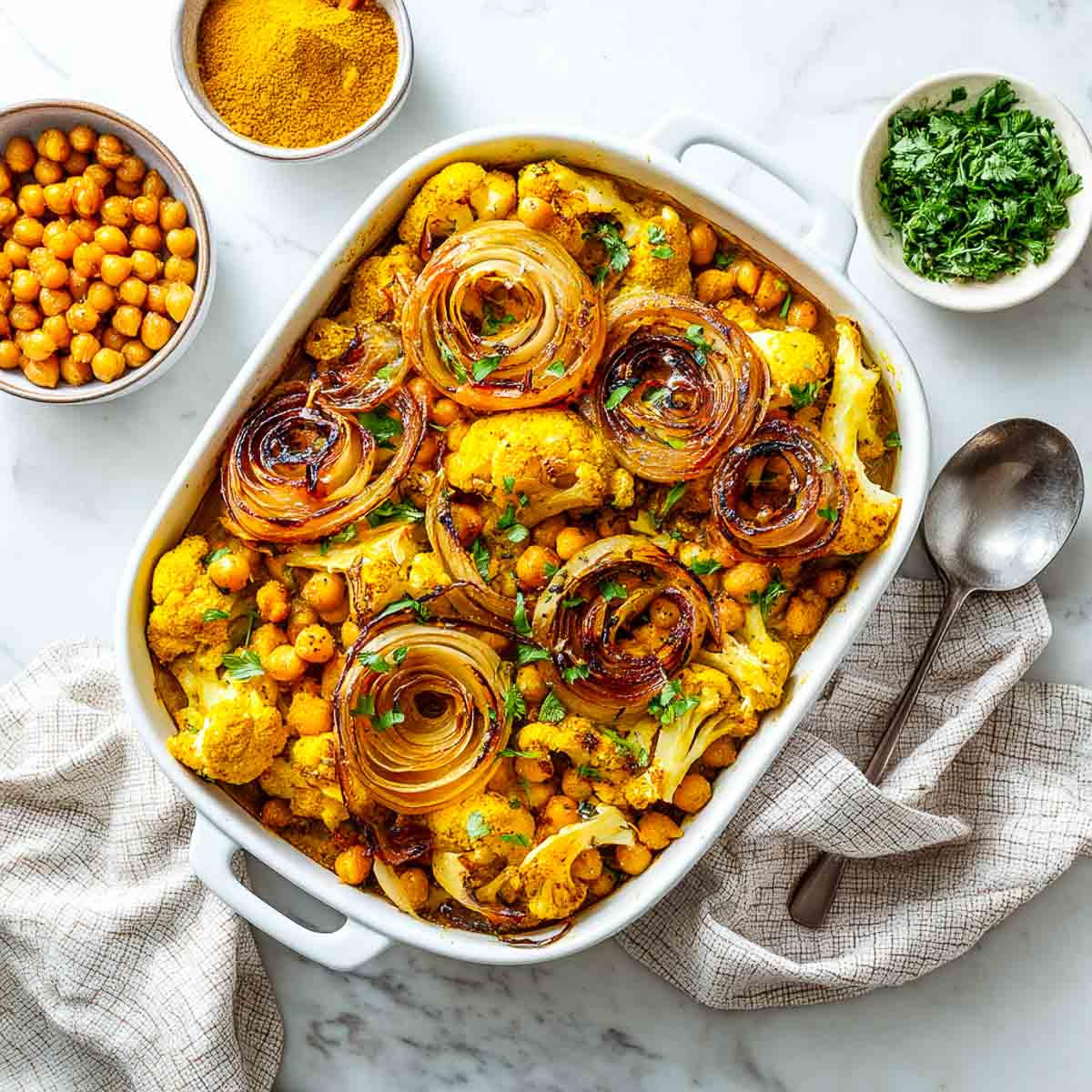 Full cauliflower and chickpea casserole topped with golden rosette onions in a white baking dish.