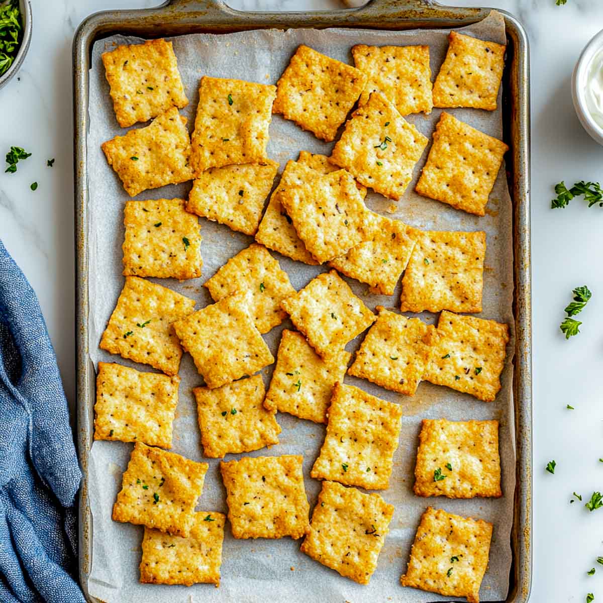 Top-down view of almond flour crackers on baking tray with parsley garnish.