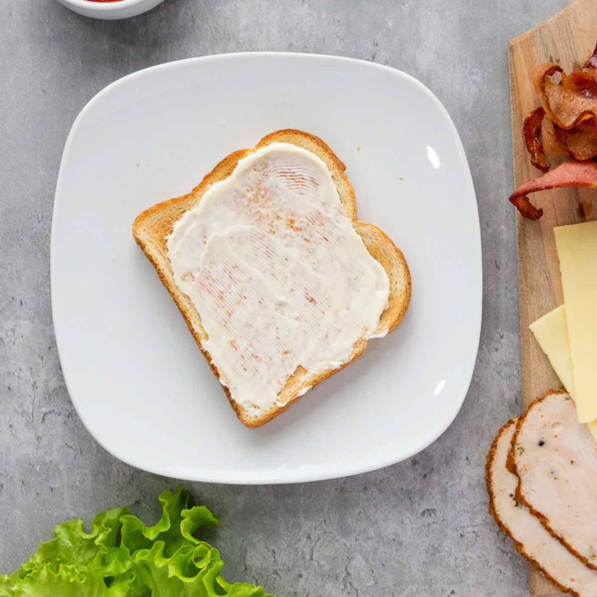 Mayonnaise spread on the first layer of toasted bread.