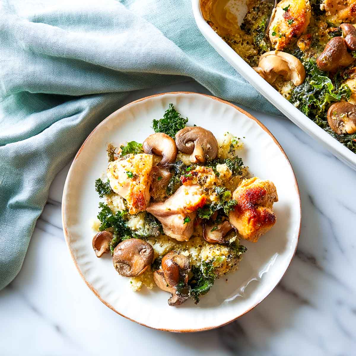 Chicken and kale casserole with mushrooms and cauliflower rice in white baking dish.