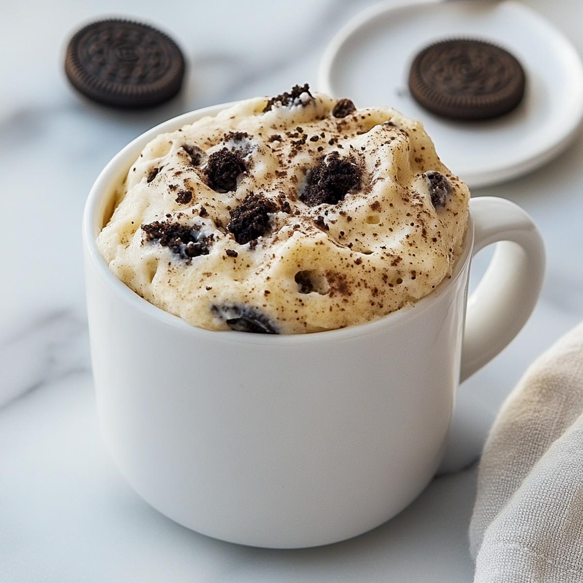 Cookies and cream mug cake with Oreo crumbs in white mug and napkin.