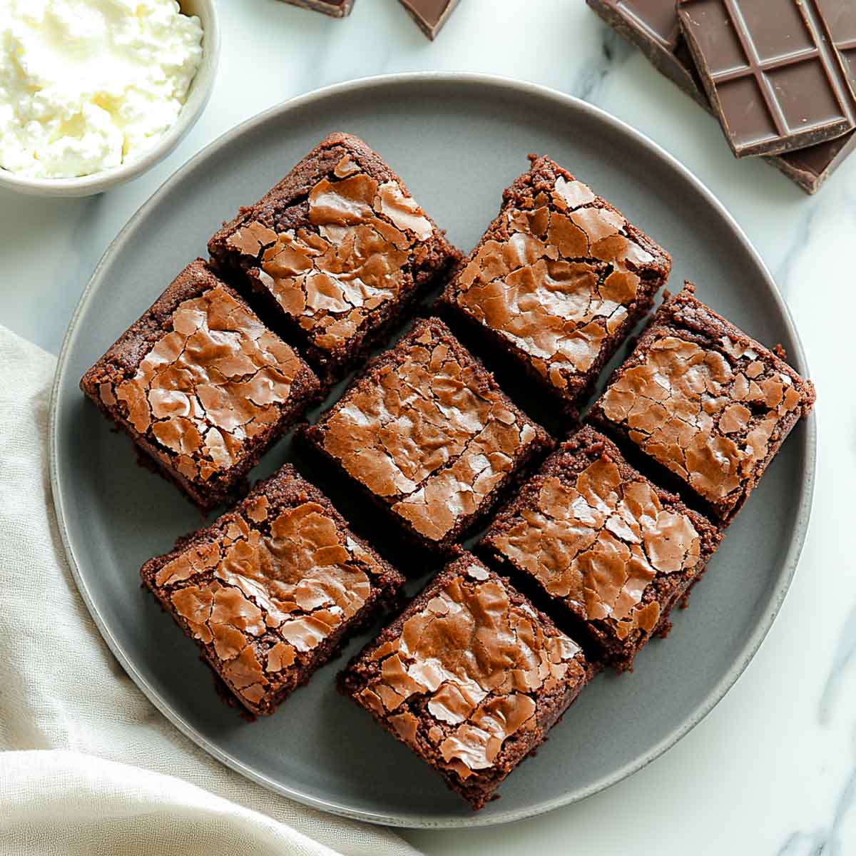 Fudgy cottage cheese brownies with crinkled tops on charcoal grey plate.