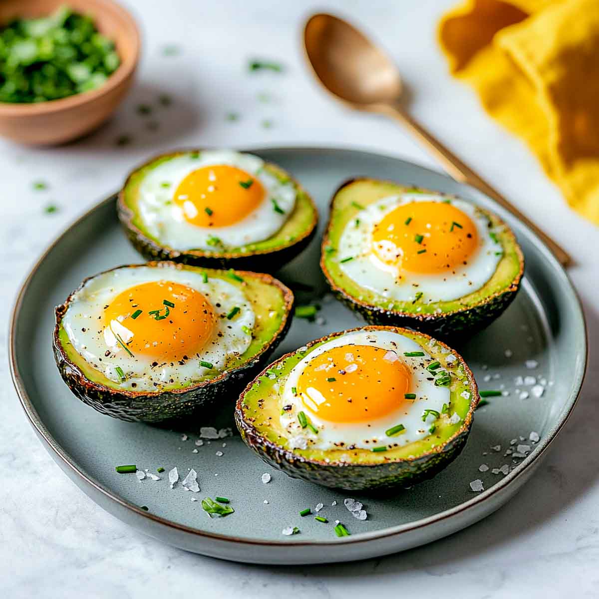 Baked eggs nestled inside avocado halves, garnished with chives and flaky salt.