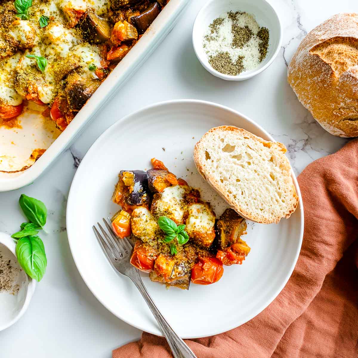 Cheesy eggplant and tomato casserole served with crusty artisan bread and basil.
