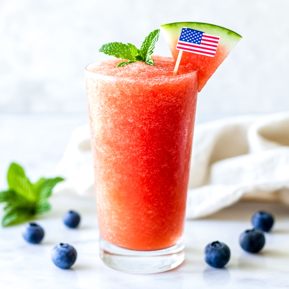 A glass of watermelon slush on a white marble surface.