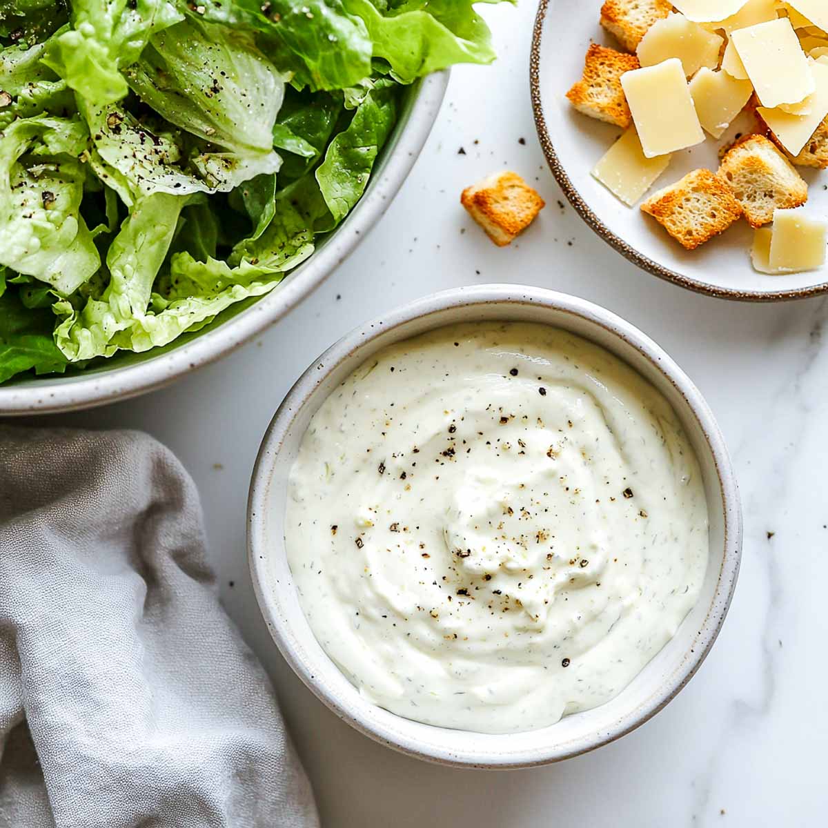 Small bowl of creamy garlic parmesan Greek yogurt dressing on marble.