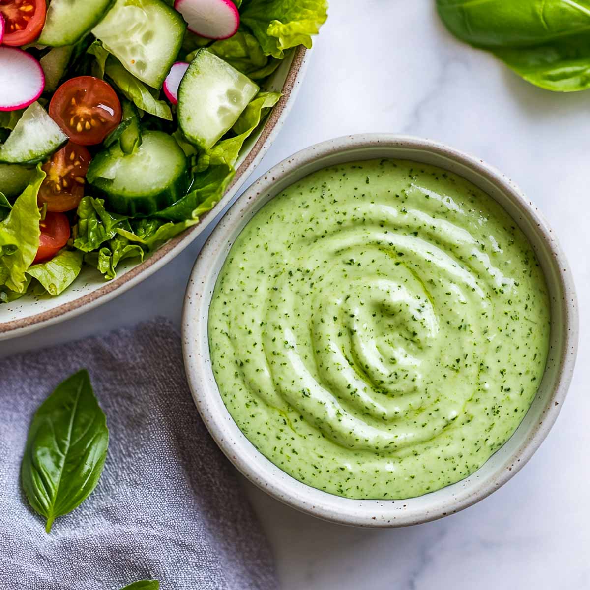 Green goddess Greek yogurt dressing with chopped salad and basil leaves.