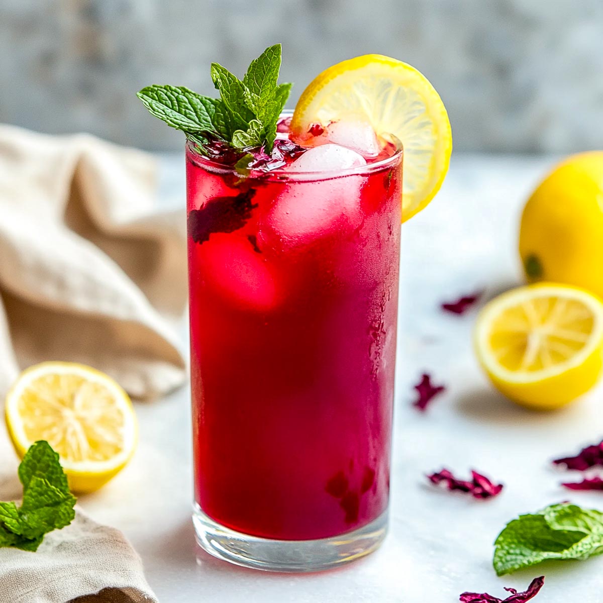 Deep red hibiscus lemonade with mint and lemon wheel in a tall glass.