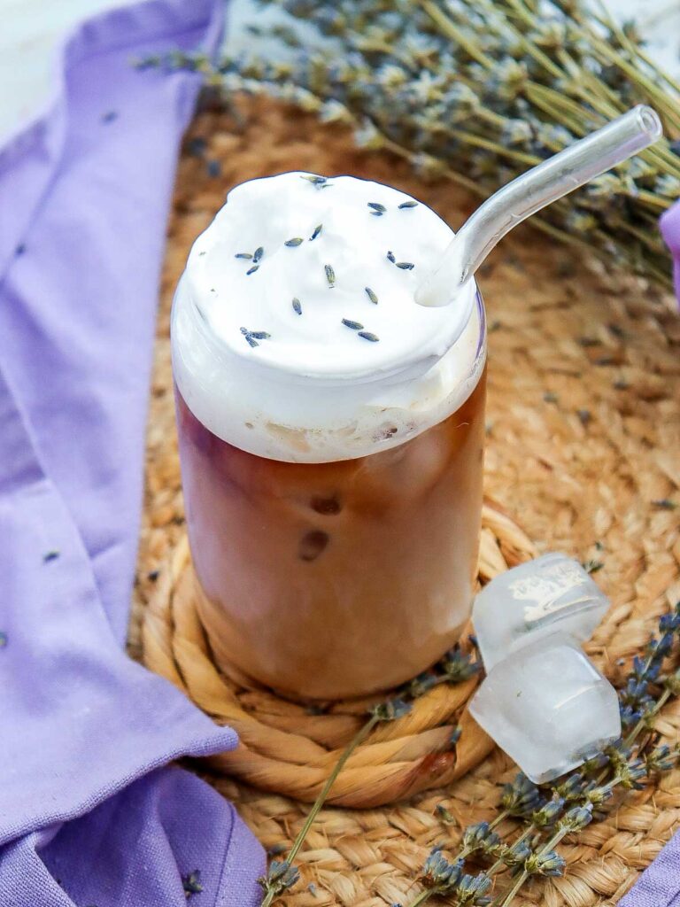 Slightly angled view of a glass of lavender iced coffee served with a straw.
