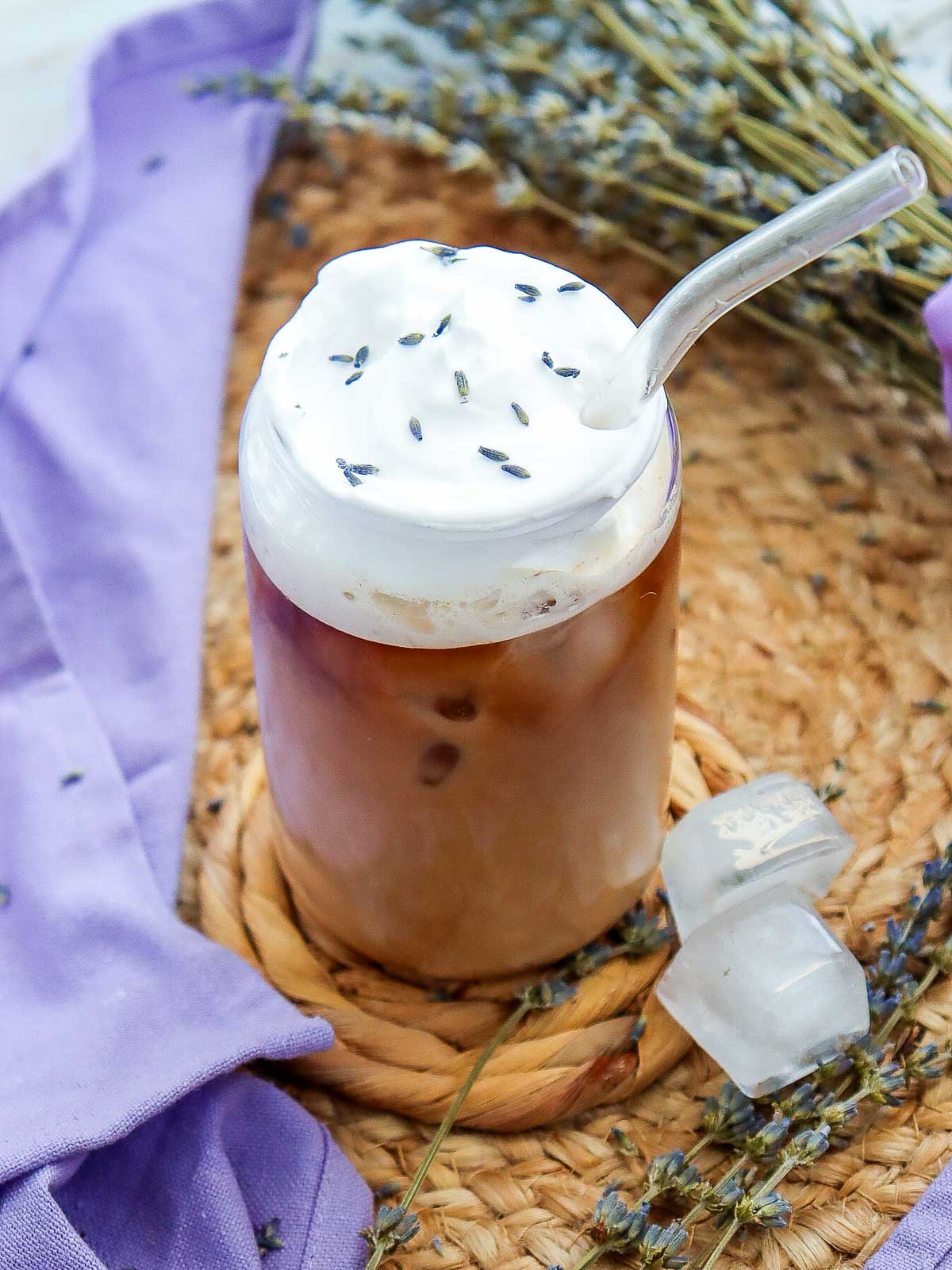 Slightly angled view of a glass of lavender iced coffee served with a straw.