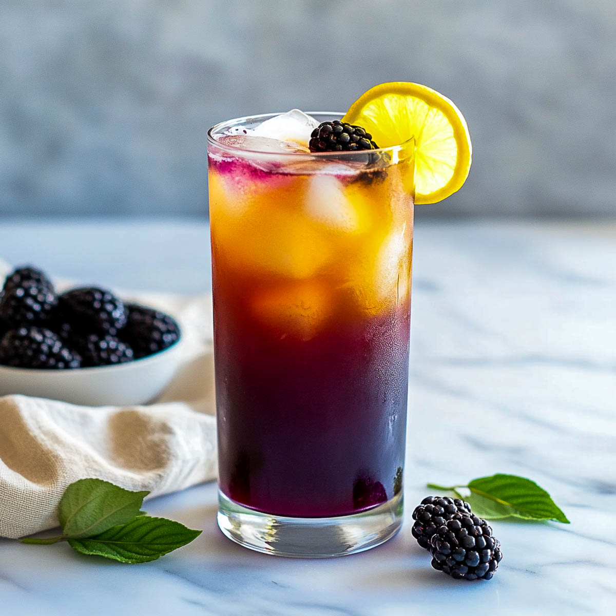 Layered iced tea with blackberries, lemon verbena, and lemon slice in a tall glass.