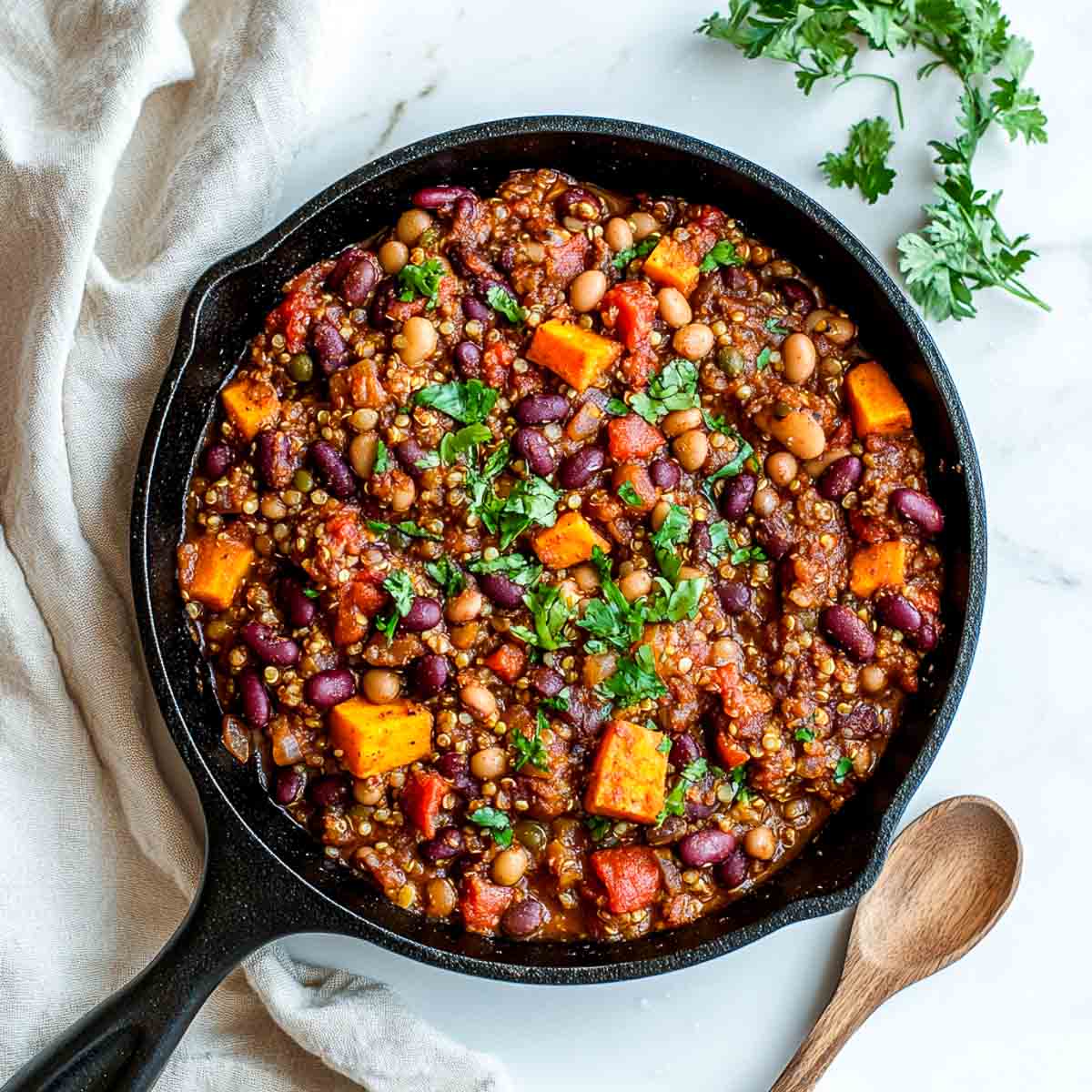 Lentil quinoa chili in a cast iron skillet with a wooden spoon in the side.
